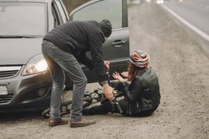Person assisting an injured cyclist on the ground beside a car after a collision, reflecting the bicycle accident matters Aulsbrook Car & Truck Wreck Injury Lawyers Fort Worth handles